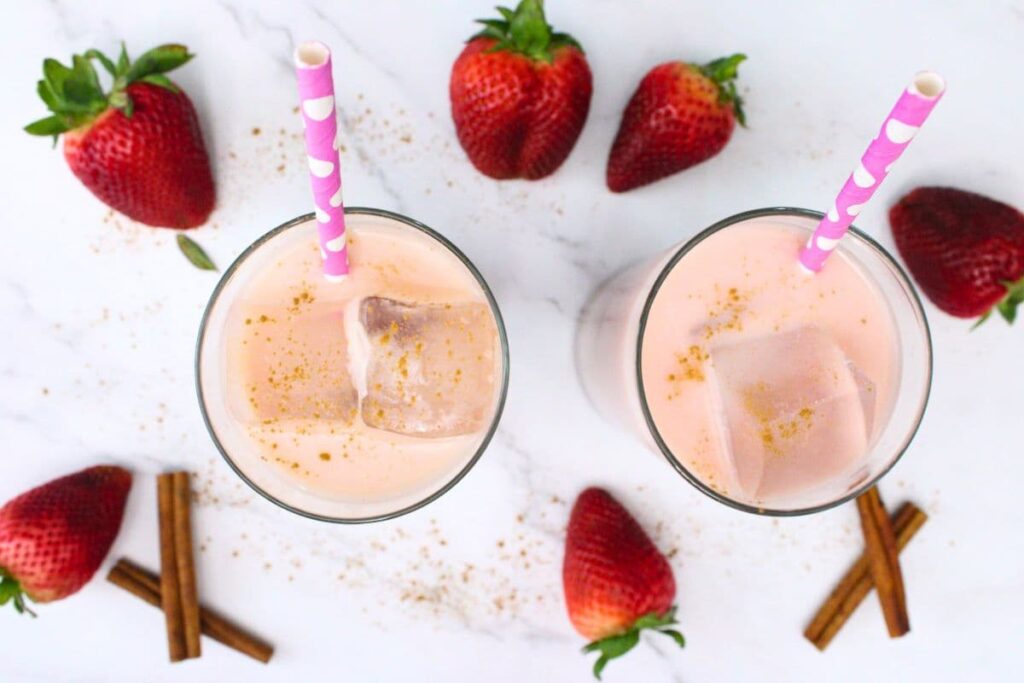 overhead view of two glasses filled with strawberry horchata chai surrounded by fresh strawberries