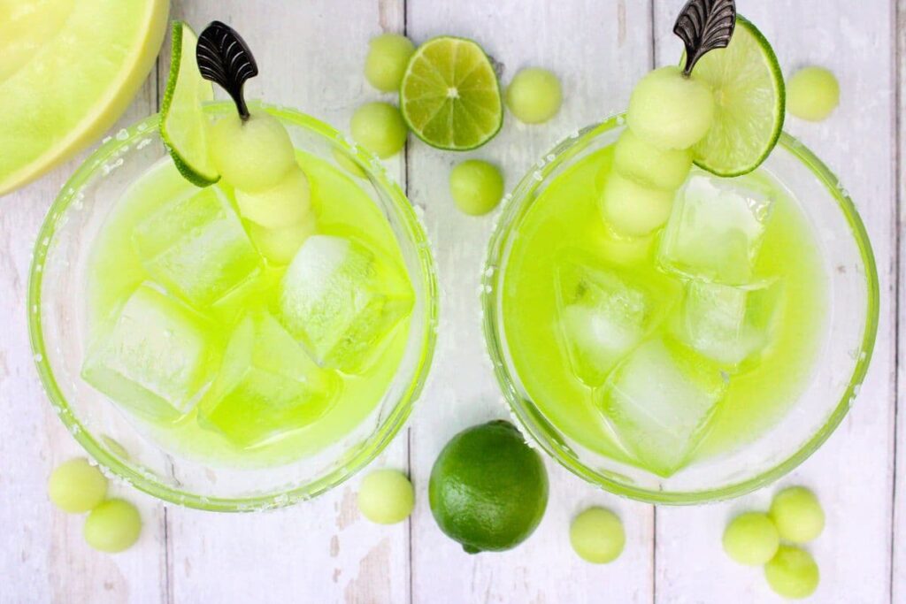 overhead view of two midori margaritas with fresh lime and melon balls