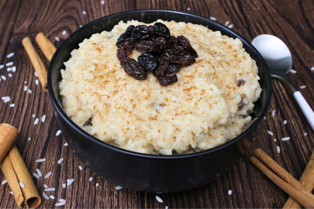 rice pudding topped with raisins in a black bowl on a wooden table