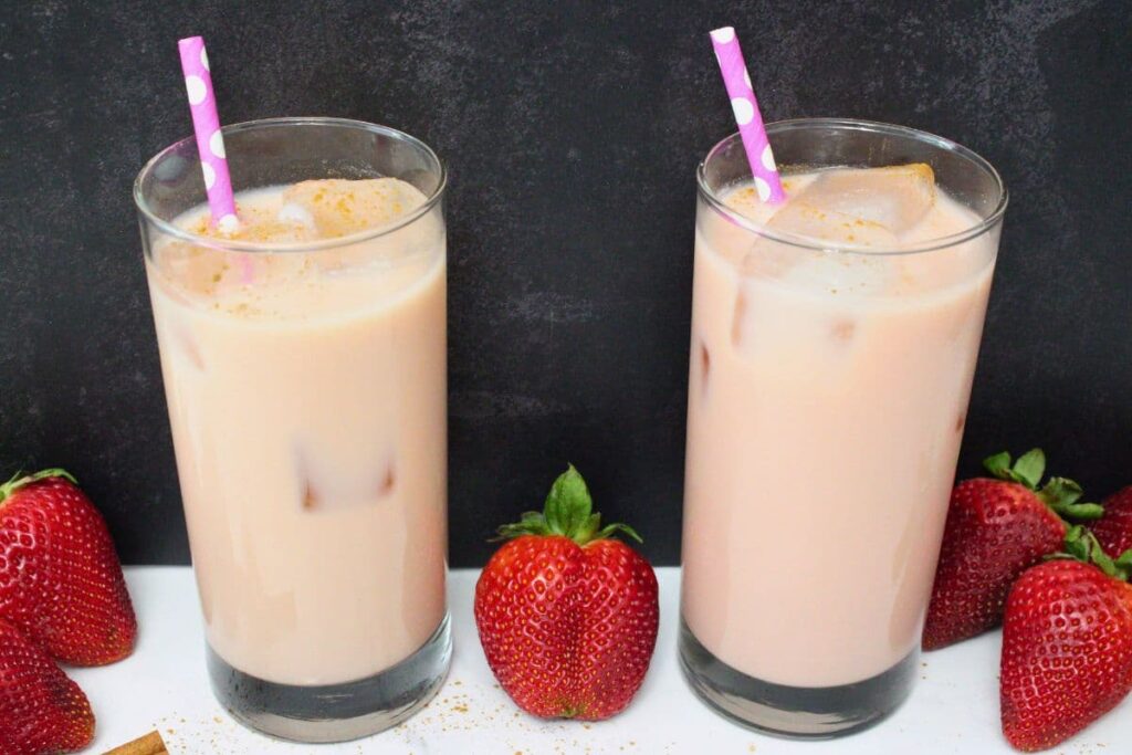 strawberry horchata chai drinks against a dark background with fresh fruit surrounding
