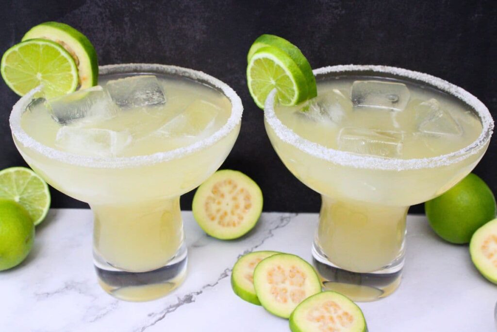 two guava margarita cocktails with fresh lime and guava against a dark background