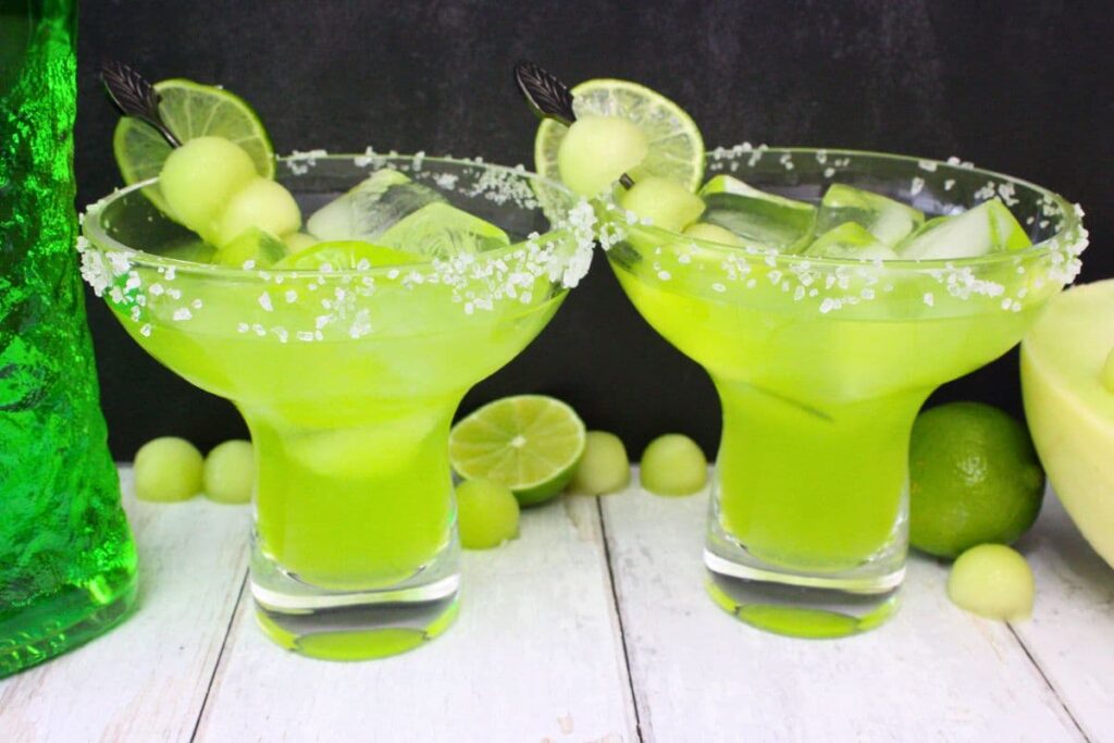 two midori margaritas with fresh fruit against a dark background