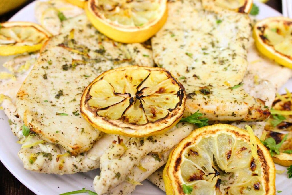 closeup view of air fryer lemon chicken on a plate with charred lemon slices