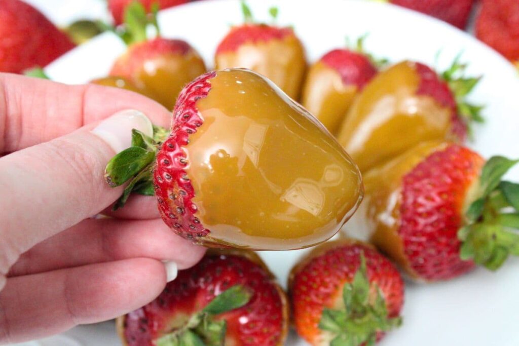 holding up a caramel coated strawberry