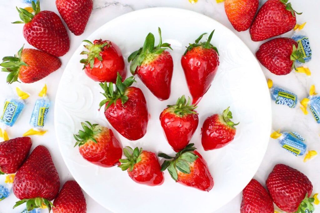 overhead view of jolly rancher candy coated strawberries on a white plate