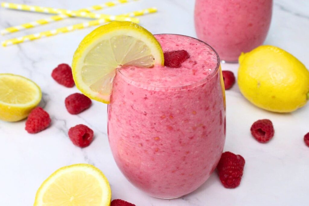 raspberry lemonade smoothie drink on a white countertop surrounded by fruit and straws