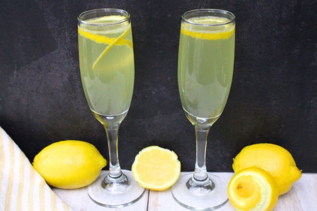 two champagne flutes filled with limoncello french 75 cocktail against a dark background