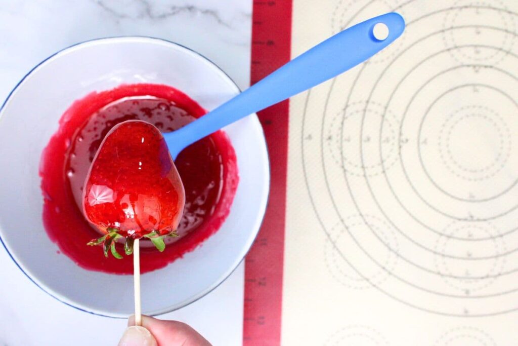 use the toothpick to dip the strawberries in the melted jolly rancher candy