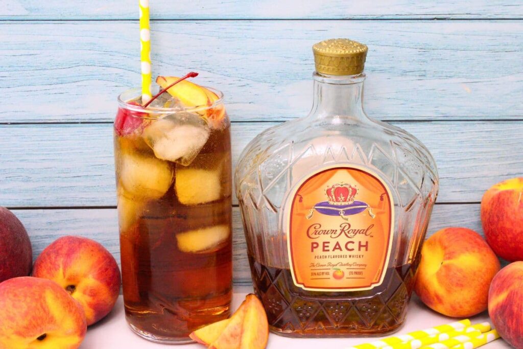 crown peach and cream soda cocktail next to crown royal peach whisky bottle in front of light wood background