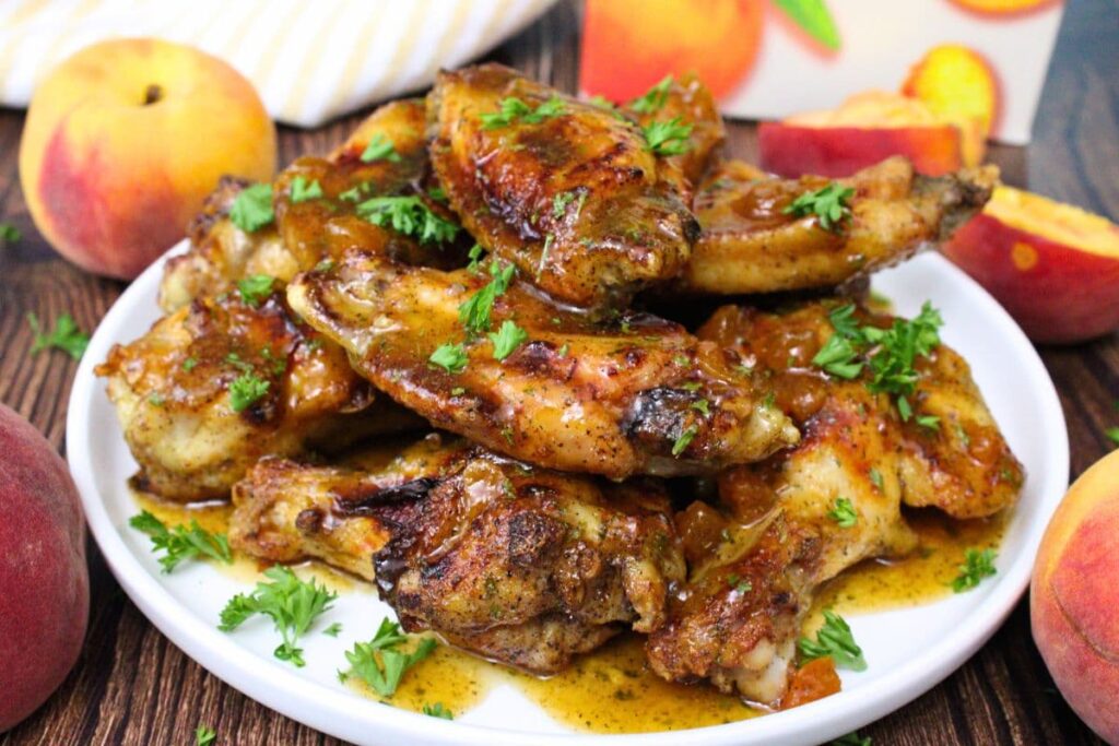 crown royal peach wings made in the air fryer stacked up on a plate surrounded by peaches