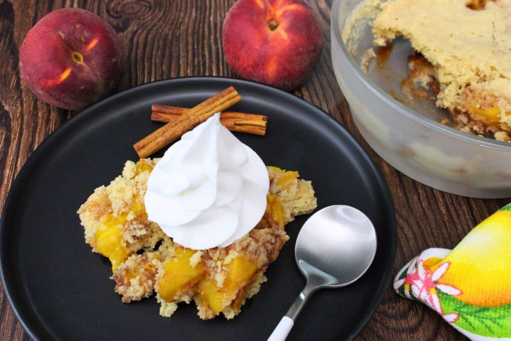 microwave peach cobbler on a plate with whipped cream on top