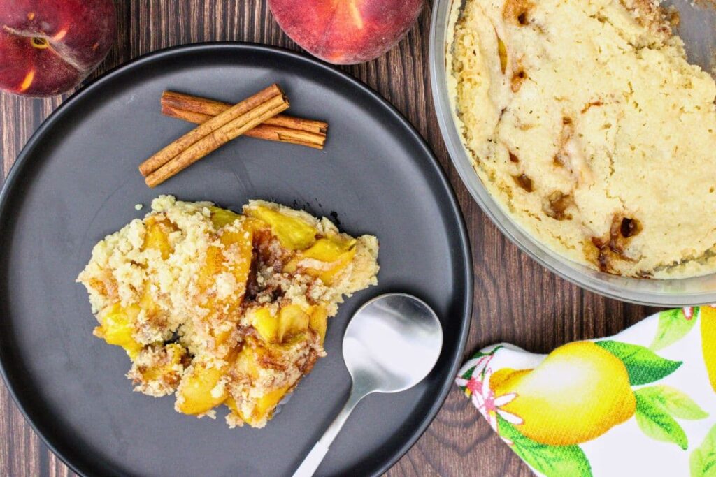 overhead view of microwave peach cobbler on a black plate with a spoon to the side