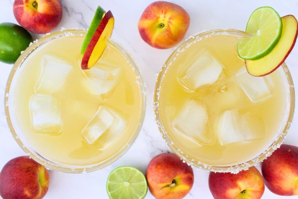 overhead view of two crown peach margaritas on the rocks with peach and lime on the rim