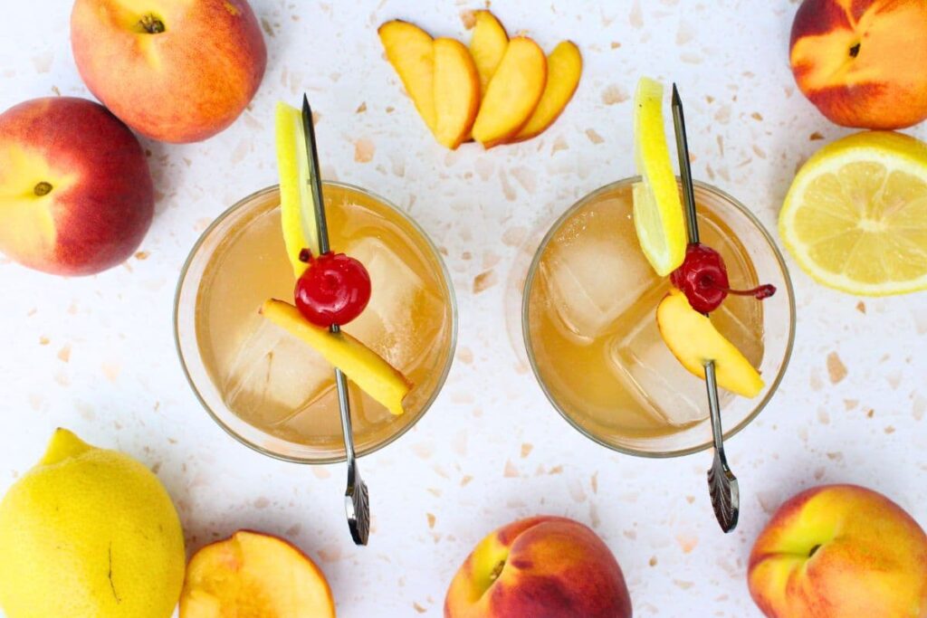 overhead view of two crown peach whiskey sour drinks with a skewer of lemon, peach, and cherry