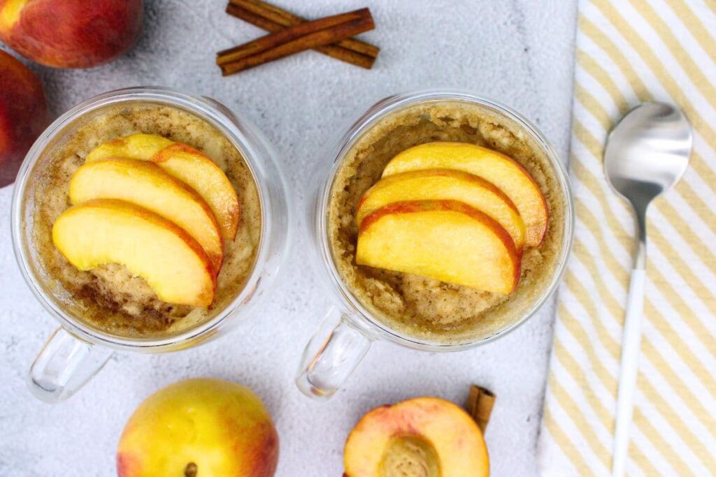 overhead view of two peach mug cake with fresh peach slices on top