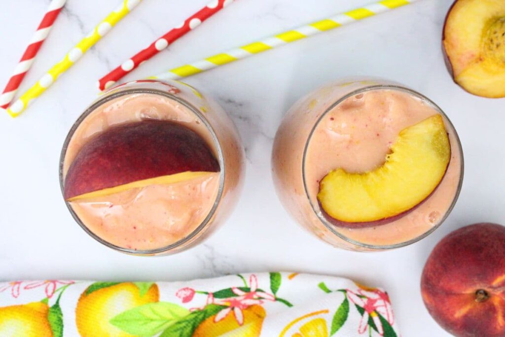 overhead view of two peach strawberry mango smoothie drinks with fresh peach on top