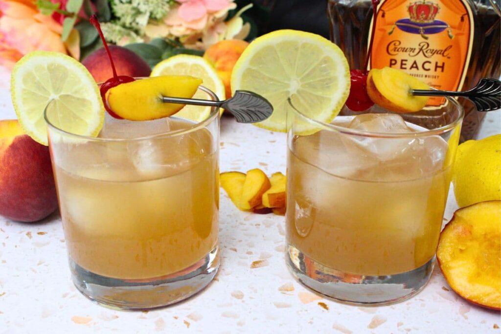 two peach whiskey sour cocktails sitting in front of a crown royal bottle