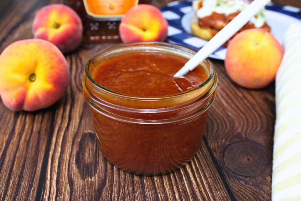 jar of homemade whiskey peach bbq sauce with a spoon handle sticking out