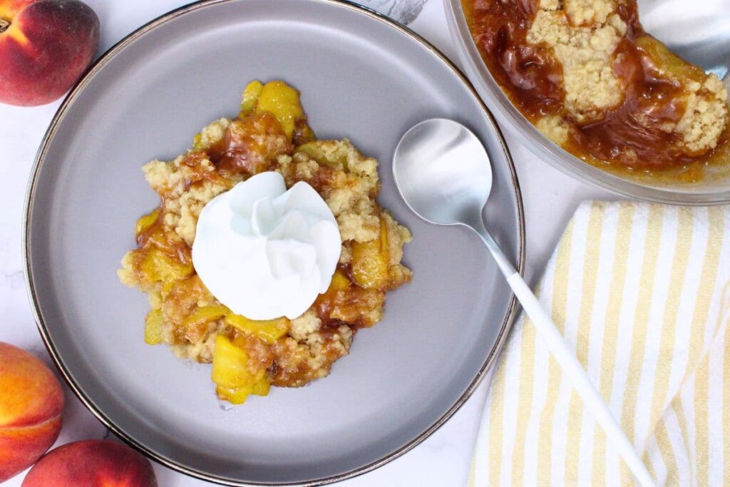overhead view of microwave peach crumble on a plate with a spoon and topped with whipped cream