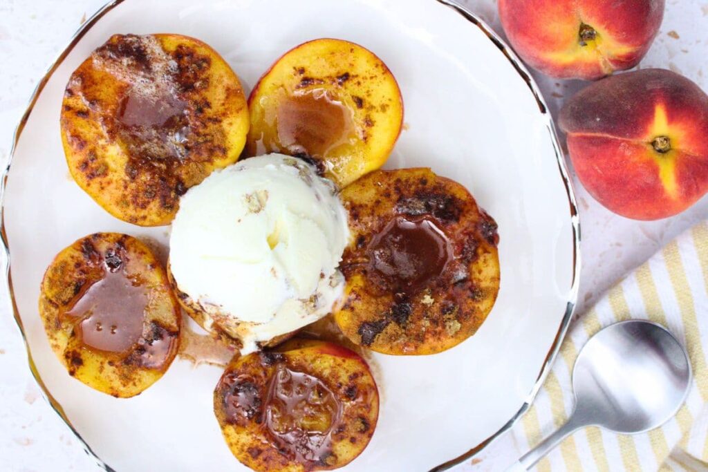 overhead view of several halves of microwave baked peaches on a plate topped with ice cream