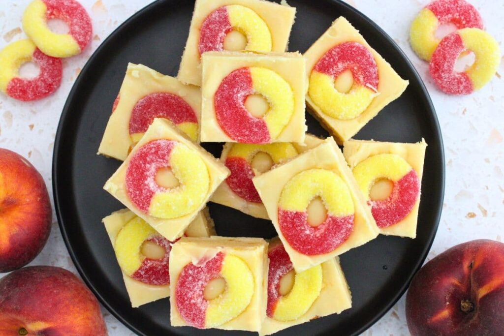 overhead view of squares of homemade peach fudge on a black plate with peach rings on top