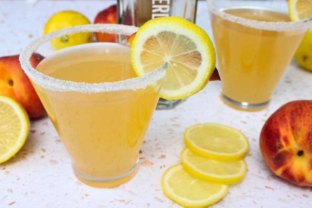 peach lemon drop martini with a lemon slice garnish in front of the vodka bottle