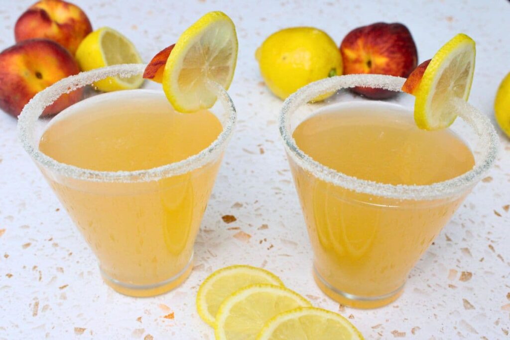 two peach lemon drop martinis side by side with a lemon slice garnish