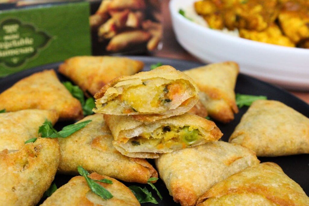 air fryer trader joes vegetable samosas on a plate with one cut in have to show the inner filling