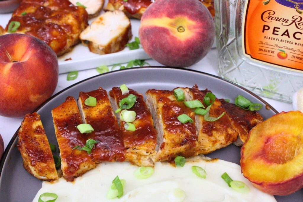 peach whiskey bbq chicken breast slices spread across a plate with mashed potatoes