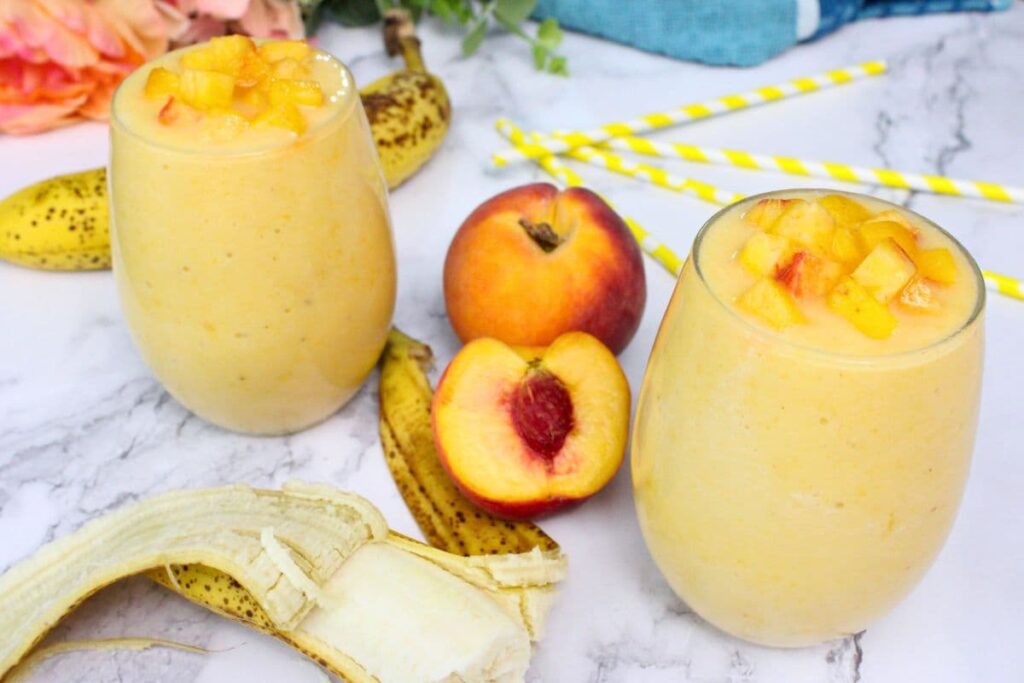 two peach banana smoothie drinks with fresh cut peaches and banana in between