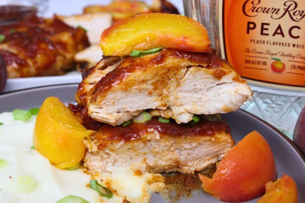 two slices of peach whiskey bbq chicken on top of each other topped with a peach slice