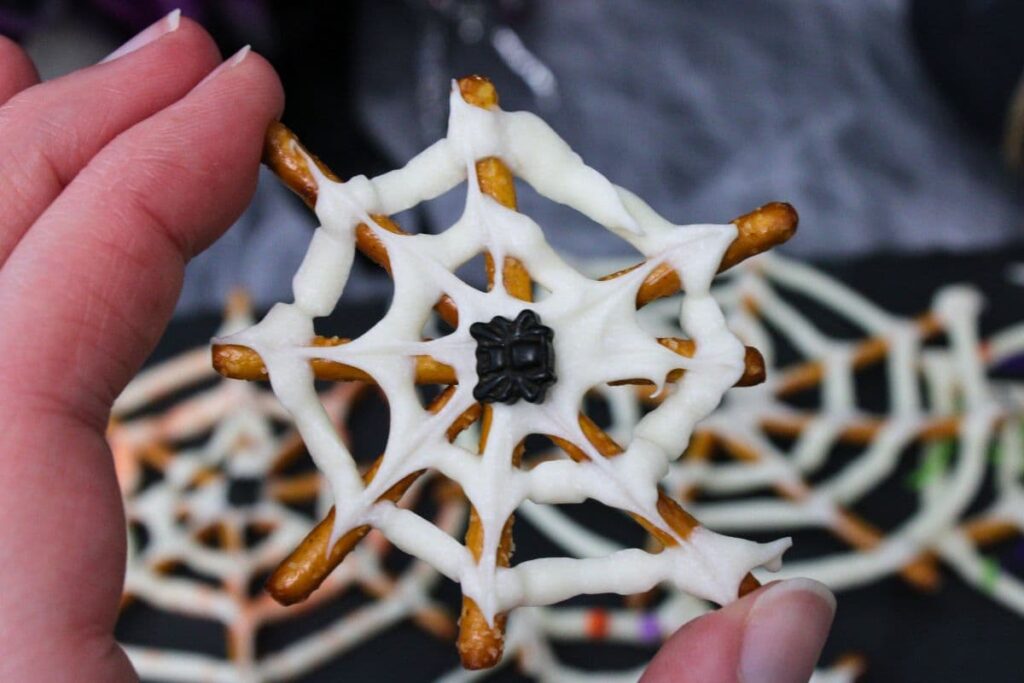 holding up a bite size version of a chocolate spider web pretzel