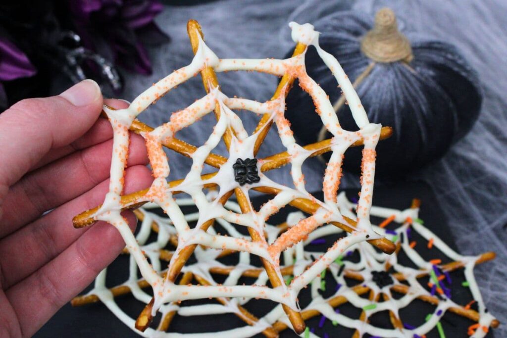 holding up a white chocolate spider web pretzel with orange sugar sparkles