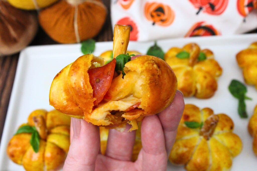 holding up an air fryer pizza pumpkin split in half to show the pepperoni and cheese inside
