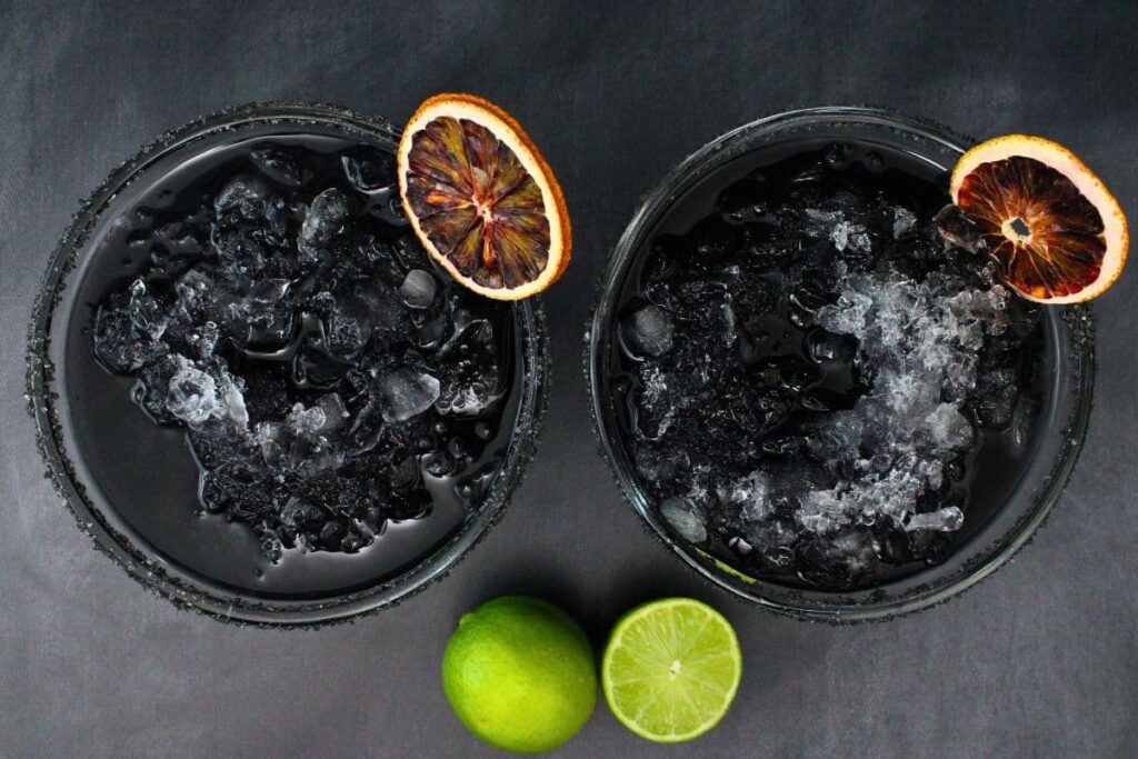 overhead view of two black margaritas garnished with dried blood orange slices with fresh limes