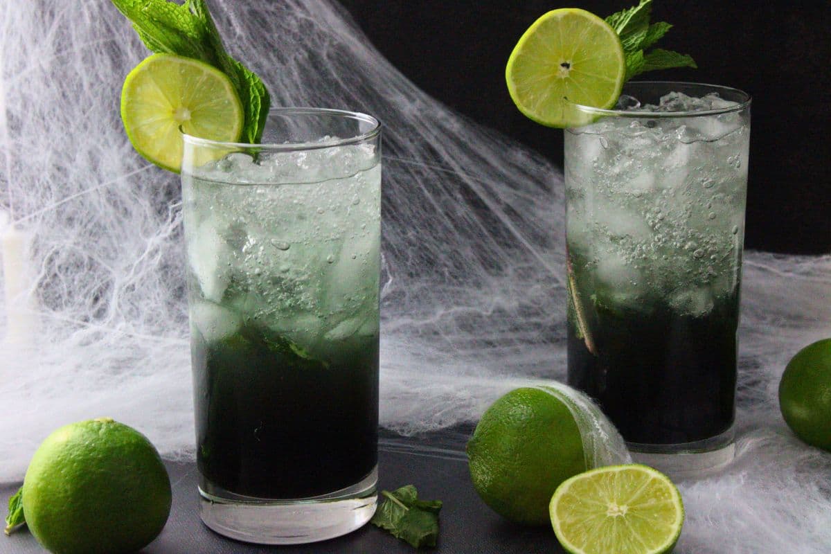 two black mojito cocktails in front of spiderwebs with fresh limes