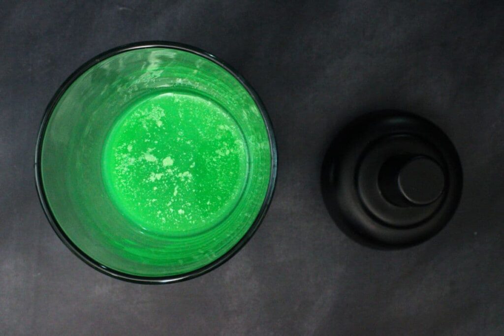 add vodka, midori, blue curacao, orange juice, and green luster dust to cocktail shaker