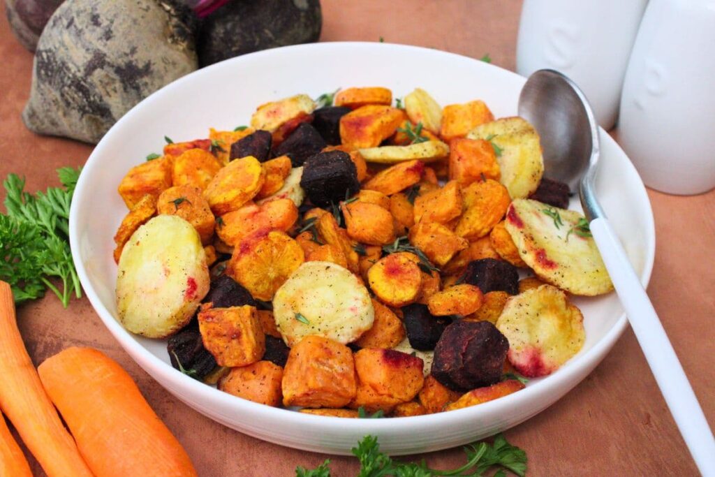 bowl of air fryer root vegetables with a spoon surrounded by fresh beets and carrots