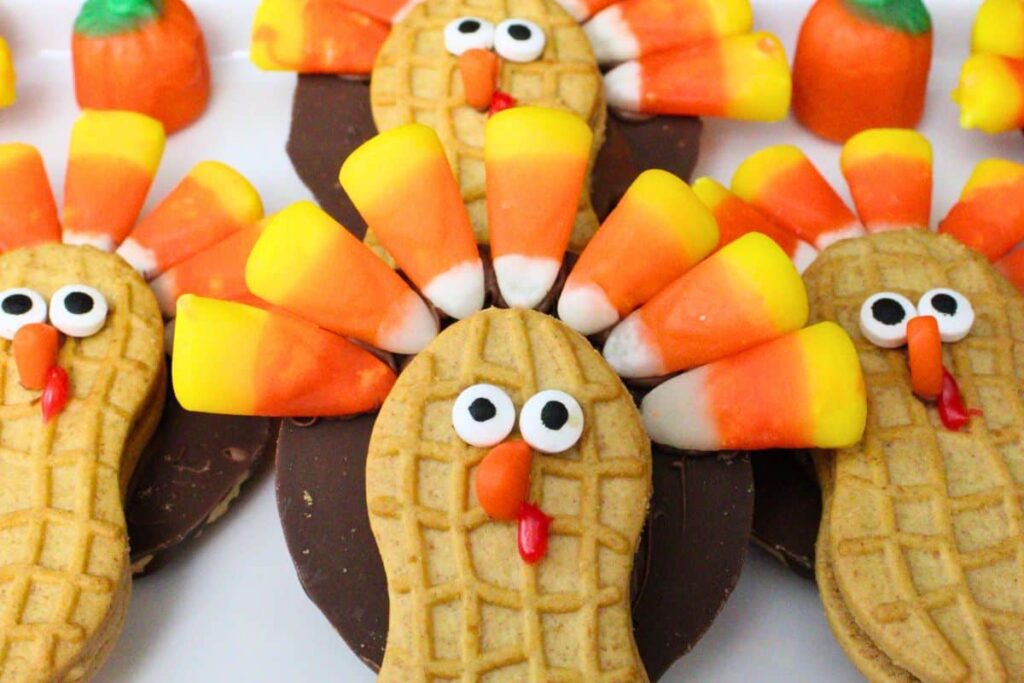 closeup of four nutter butter turkey cookies looking at the camera with candy corn headdresses