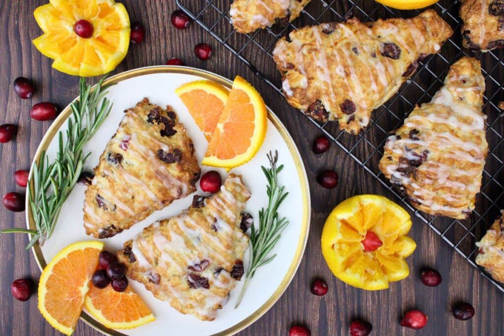 overhead view of air fryer cranberry orange scones on a plate and wire rack surrounded by orange and cranberries