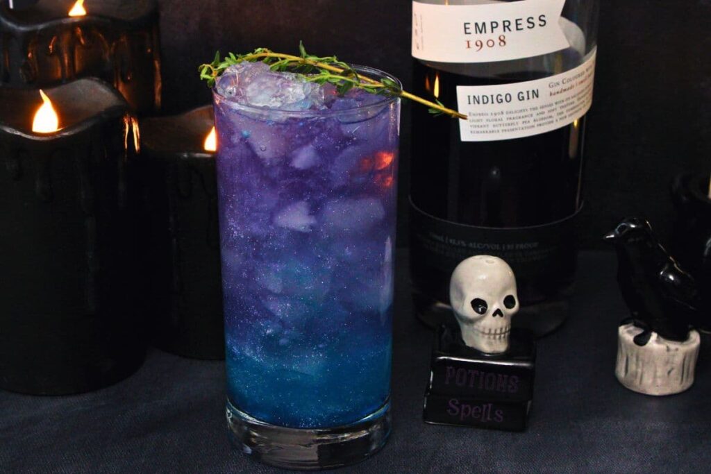 shimmering hocus pocus cocktail in front of indigo gin bottle