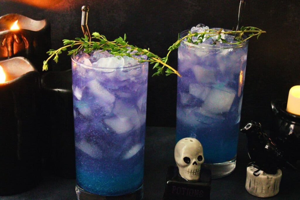 two hocus pocus cocktails garnished with thyme and crooked stirrers