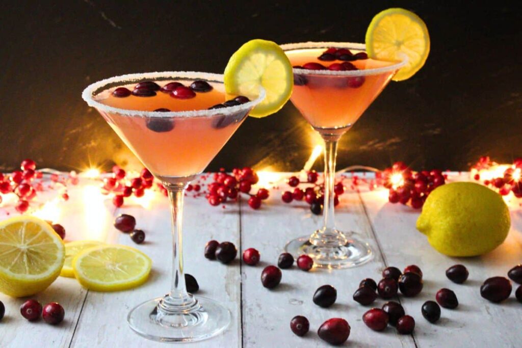 two cranberry lemon drop martinis surrounded by fresh fruit and christmas lights