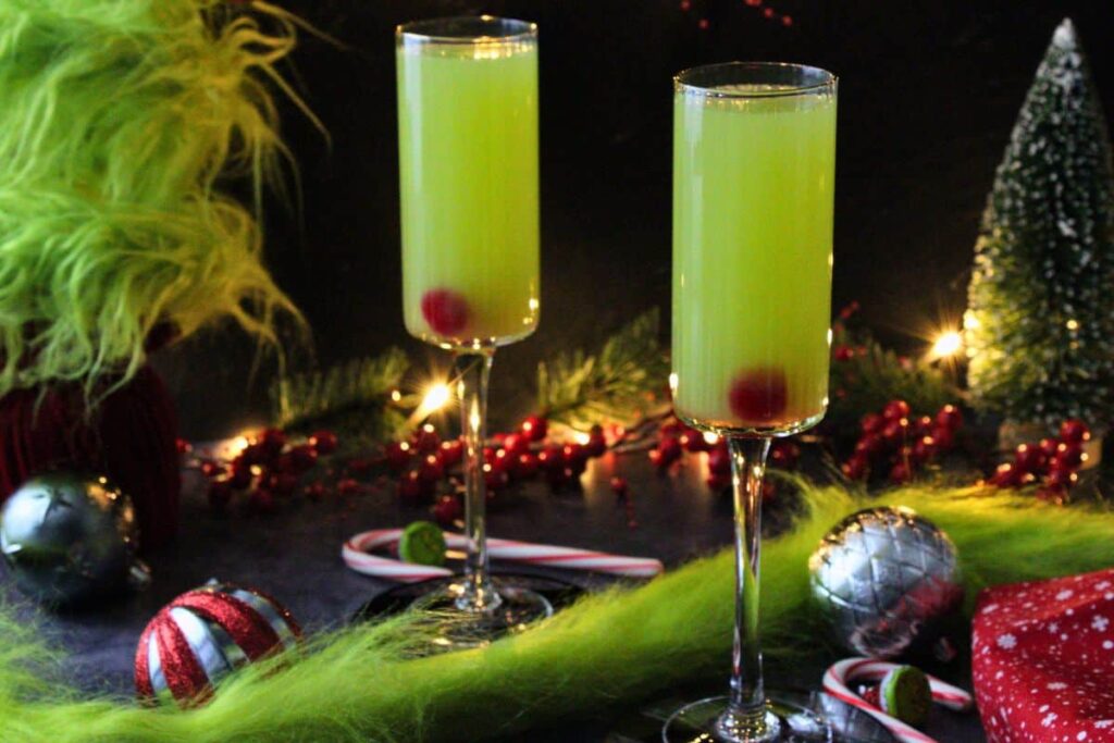 two grinch mimosas in a holiday scene with christmas lights, ornaments, and grinch garland
