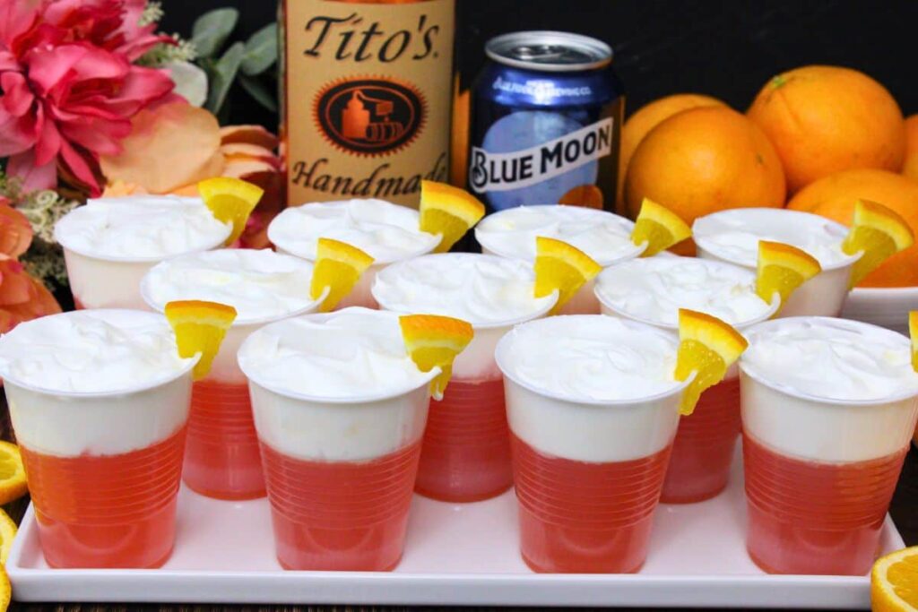 blue moon jello shots topped with cool whip in front of beer can and vodka bottle