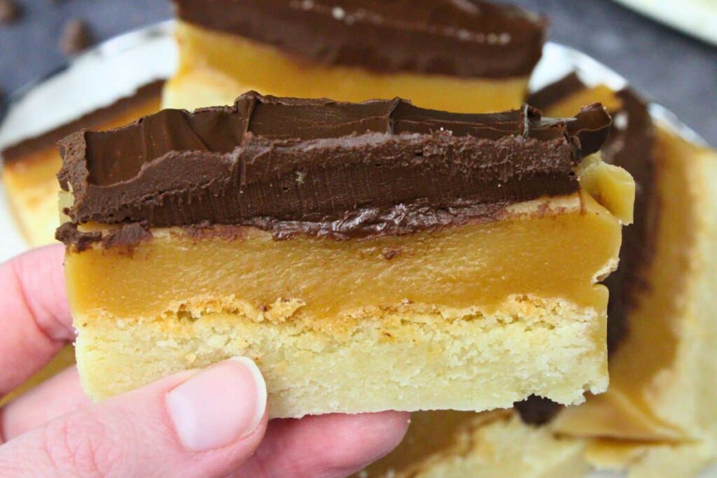 holding up a slice of air fryer millionaire shortbread showing chocolate and caramel layers