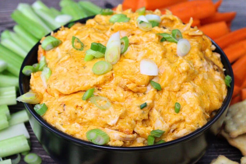 microwave buffalo chicken dip in a black bowl surrounded by carrots celery and crackers