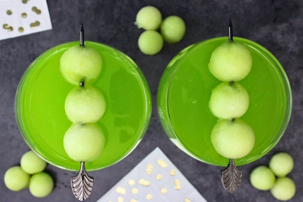overhead view of two melon ball drop cocktails with a skewer of fresh melon balls