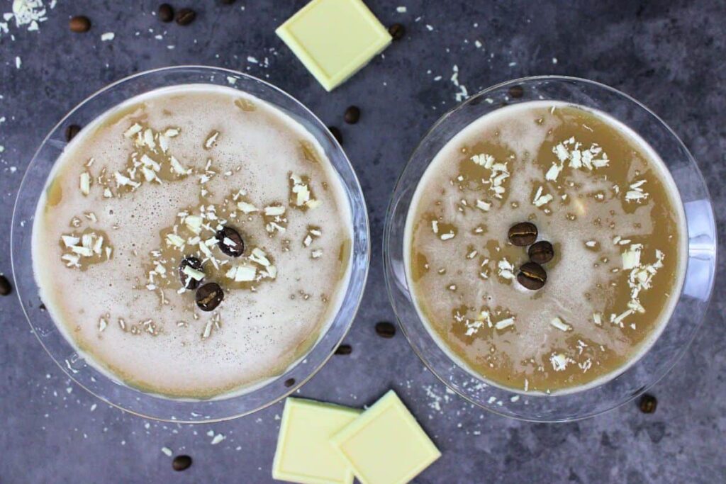 overhead view of two white chocolate espresso martinis with three coffee beans each and chocolate shavings