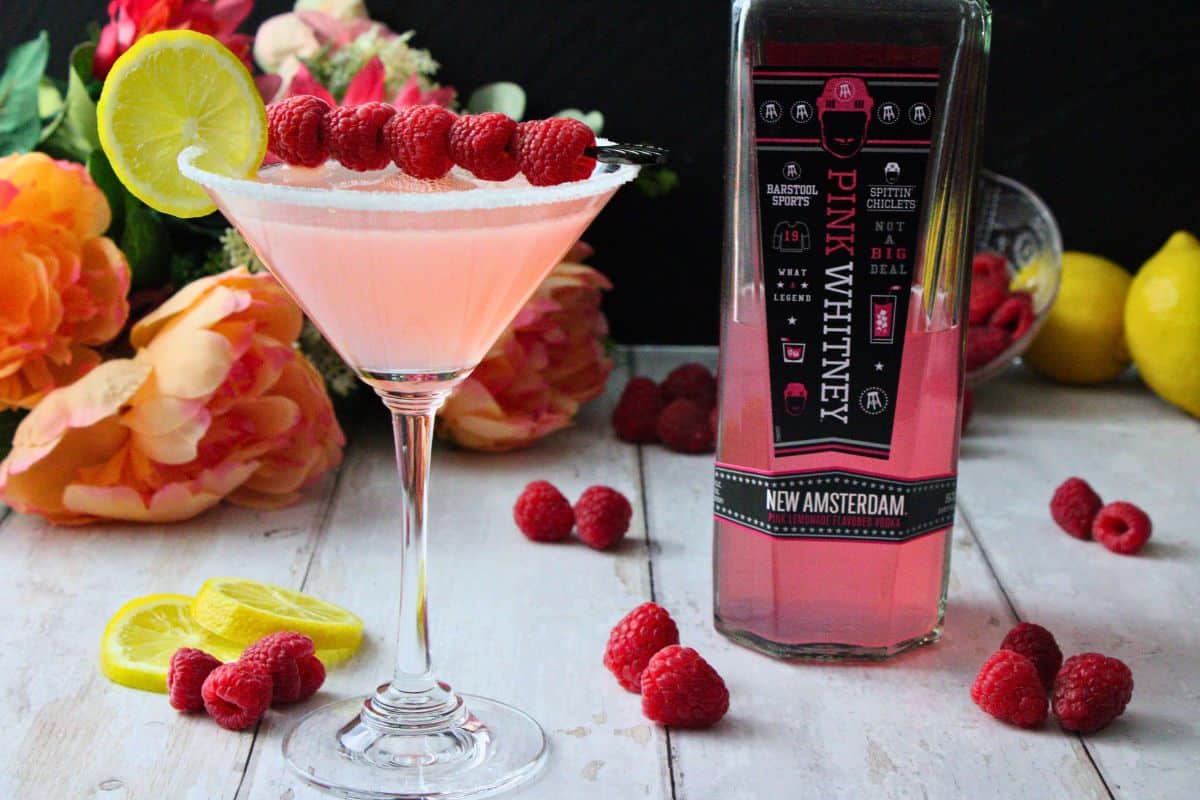 pink lemon drop martini garnished with fresh fruit next to pink whitney bottle